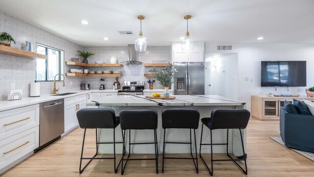 A modern kitchen with a central island, bar stools, stainless steel appliances, and a flat-screen TV.
