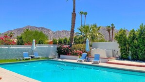 Une piscine entourée de chaises longues et de parasols, bordée de palmiers et avec une chaîne de montagnes en toile de fond.