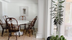 Un coin repas avec une table et des chaises blanches, un luminaire suspendu et une plante en pot près de la fenêtre.