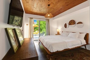 Relax in this serene bedroom with a large bed, wooden ceiling, and a view of lush greenery outside.