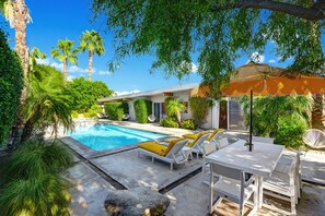 A pool area with lounge chairs and a table, surrounded by greenery and palm trees. - Sol House - Midcentury, Pool & Spa, Views! (Palm Springs)