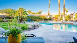 A pool area with a curved design, surrounded by palm trees and a well-maintained lawn. - Palmeras- Pool, Views, Game Room (Indian Wells)