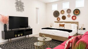 A modern bedroom with a bed, bedside tables, a TV, and decorative wall art. - Modern Wanderlust - Pool - Spa -Views - 3B2B259320 (La Quinta)