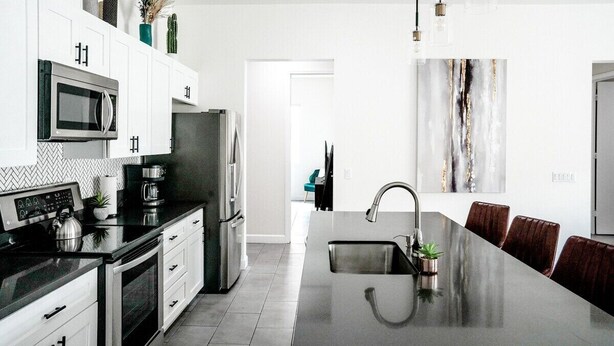 A modern kitchen with white cabinetry, stainless steel appliances, and a central island with a sink. - Modern Wanderlust - Pool - Spa -Views - 3B2B259320 (La Quinta)