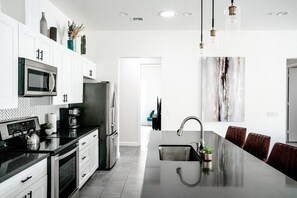 A modern kitchen with white cabinets, stainless steel appliances, and a central island with a sink. - Modern Wanderlust - Pool - Spa -Views - 3B2B259320 (La Quinta)