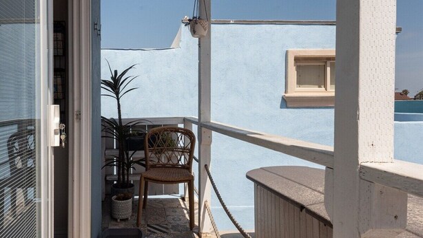 Un balcón con piso estampado, una silla de mimbre, una planta en maceta y vista al mar.