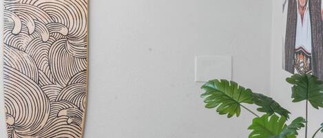 Paret amb una taula de surf de fusta, un penjallum, un quadre amb marc i una planta en test.