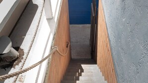 Unos escalones de hormigón bajan hacia una pared azul, con una barandilla blanca a la izquierda y una cuerda atada a un poste de metal.