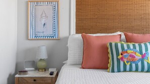 Une chambre à coucher avec un lit, des oreillers, une table de chevet, une lampe et des œuvres d’art encadrées accrochées au mur.