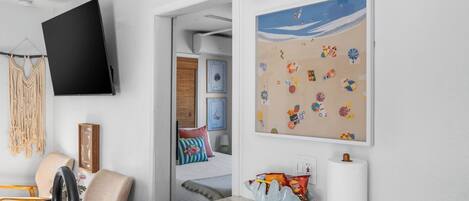 A modern living room with a flat-screen TV, a macrame wall hanging, a beach-themed artwork, and a unique salt shaker.