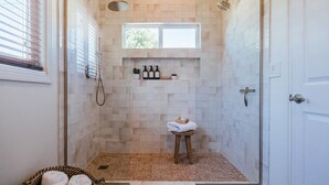 A walk-in shower with beige tiles, a small window, a shelf with toiletries, and a towel rack.
