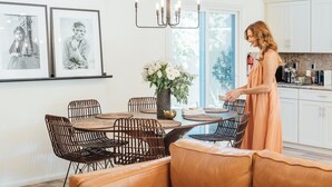 A dining area with a round table, wicker chairs, a vase with flowers, and a person standing by the table.