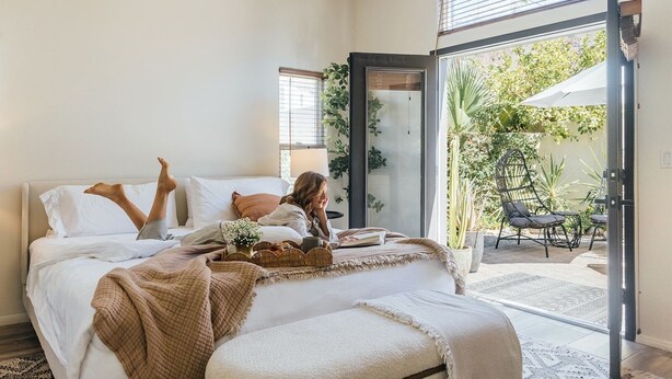 A bedroom with a bed, a bedside table, a window, and a view of the outdoors.