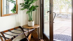 Une pièce comprenant un banc en bois, une plante en pot, un miroir et une porte-fenêtre coulissante donnant sur un espace extérieur doté d’un sol carrelé et d’un mur en pierre.