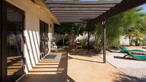 Ein überdachter Außenbereich mit Betonboden, einer Pergola und einer Sitzecke inklusive Tisch und Stühlen.
