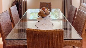 A dining area with a glass-top table surrounded by wicker chairs, a chandelier, and curtains.