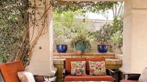 An outdoor patio area with wicker furniture, a glass table, and decorative vases.