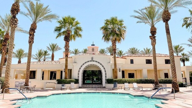 A pool area with palm trees, a building with an arched entrance, and lounge chairs.