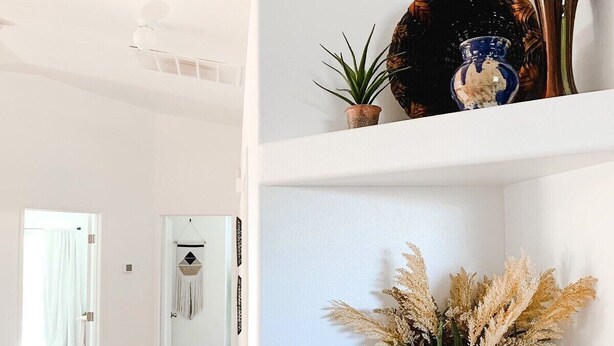 A hallway with white walls, a tiled floor, and a shelf with decorative items including a vase, a plant, and a bowl. - Desert Rose - Private Pool, Hiking, 3br, #223630 (La Quinta)