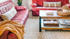 A living room with a red leather sofa, a large potted plant, and a coffee table with books and decorative items. - Desert Rose - Private Pool, Hiking, 3br, #223630 (La Quinta)
