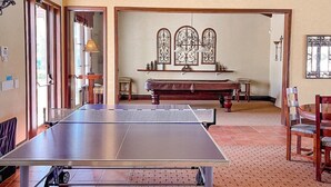 A spacious room with a ping pong table, a large window with decorative ironwork, and a wooden bench.