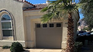 A residential building with a garage, a palm tree, and a paved driveway.