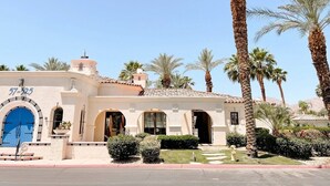 A Mediterranean-style building with a blue door, palm trees, and a clear sky.