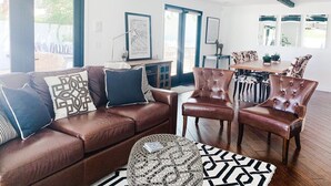 A living room with a brown leather sofa, two brown leather armchairs, a patterned coffee table, and a dining area with a table and chairs.