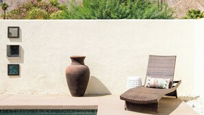 A pool area with a chair and a vase, a mountain backdrop, and a wall with framed pictures. - Carranza Cove — Private Pool, LIC #221952 (La Quinta)