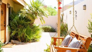 A wooden pergola with a hanging swing chair, a stone-paved patio, and a palm tree. - Carranza Cove — Private Pool, LIC #221952 (La Quinta)