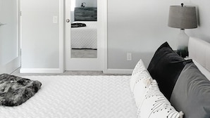 Una camera da letto con un letto, una ventola a soffitto, una lampada da comodino, un attaccapanni e uno specchio.