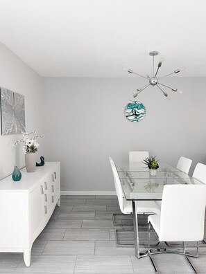 A modern dining area with a glass table, white chairs, a white cabinet, and a ceiling light fixture. - Hermosa Vista - Large Pool, Fire Pit, Scenic Views (Palm Springs)