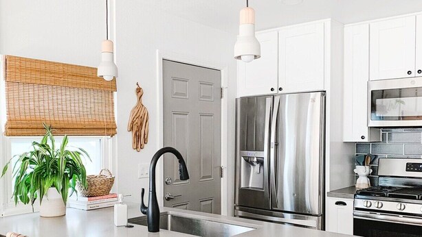 Een moderne keuken met witte kasten, roestvrijstalen apparatuur, een groot eiland met barkrukken en hanglampen.