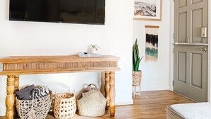 Een woonkamer met een houten tafel, een flatscreen televisie aan de muur en een deur naar een andere kamer.