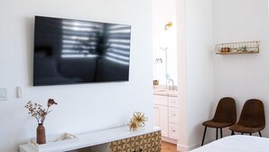 A modern bedroom with a large bed, a TV mounted on the wall, a white console table, and two chairs. - Casita Azul - Resort Amenities, Tennis 2BR260196 (La Quinta)