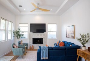 Una sala de estar con chimenea, ventilador de techo y un televisor grande montado en la pared.