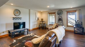 A living room with a leather couch, a TV on a stand, a windmill, and a dining area with chairs and a table. - Rustic Missouri Vacation Rental w/ Hill Views! (Greenfield)