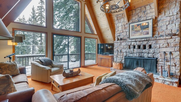 A spacious living room with a stone fireplace, large windows, and a cozy seating area. - Donner Lake Views: Rustic Truckee Cabin! (Truckee)