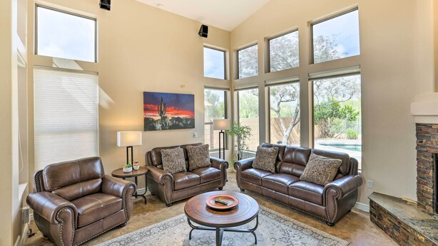 A spacious living room with leather sofas, a coffee table, and large windows offering a view of the outdoors. - Private Pool & Yard: Central Cave Creek Retreat! (Cave Creek)