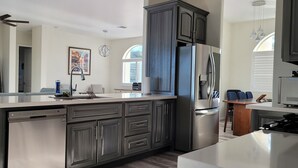 A modern kitchen with a central island, dark cabinetry, stainless steel appliances, and a dining area with blue chairs. - Casita de Tubac (Tubac)