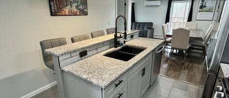 Una cocina moderna con encimeras de granito, una isla central y una zona de comedor con un sofá gris.