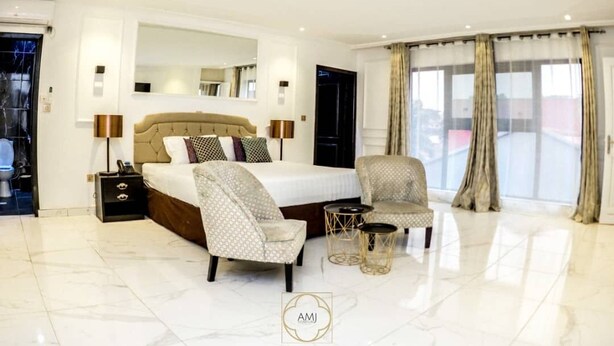 Un dormitorio amplio con una cama grande, dos sillones, una mesita de centro y un ventanal con cortinas.