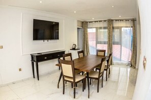 Ein Essbereich mit Holztisch und -stühlen, einem an der Wand befestigten Fernseher und Blick durch große Fenster nach draußen.