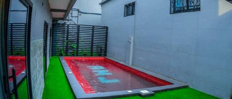 A narrow courtyard with a rectangular pool, green artificial turf, and a metal gate.
