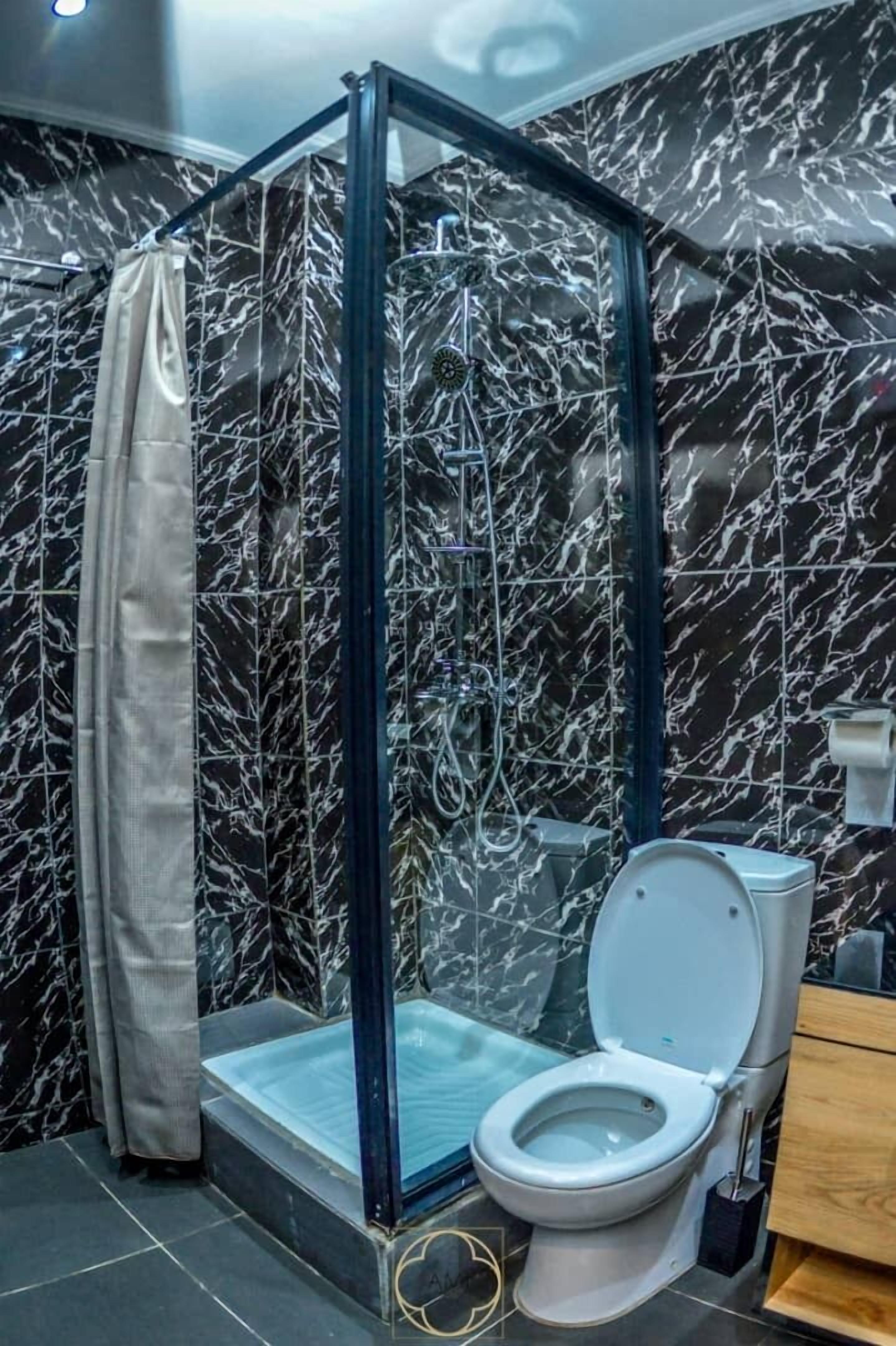 Un baño con ducha de vidrio, inodoro y paredes con diseño de mármol.