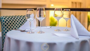 Una mesa dispuesta con cuatro copas de vino y una servilleta doblada, con un logotipo en el mantel.