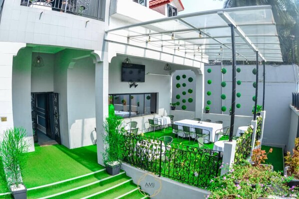 Eine moderne Außenpatio mit Glasveranda, grüner Kunstrasen und einer Sitzecke mit weißen Tischen und Stühlen.