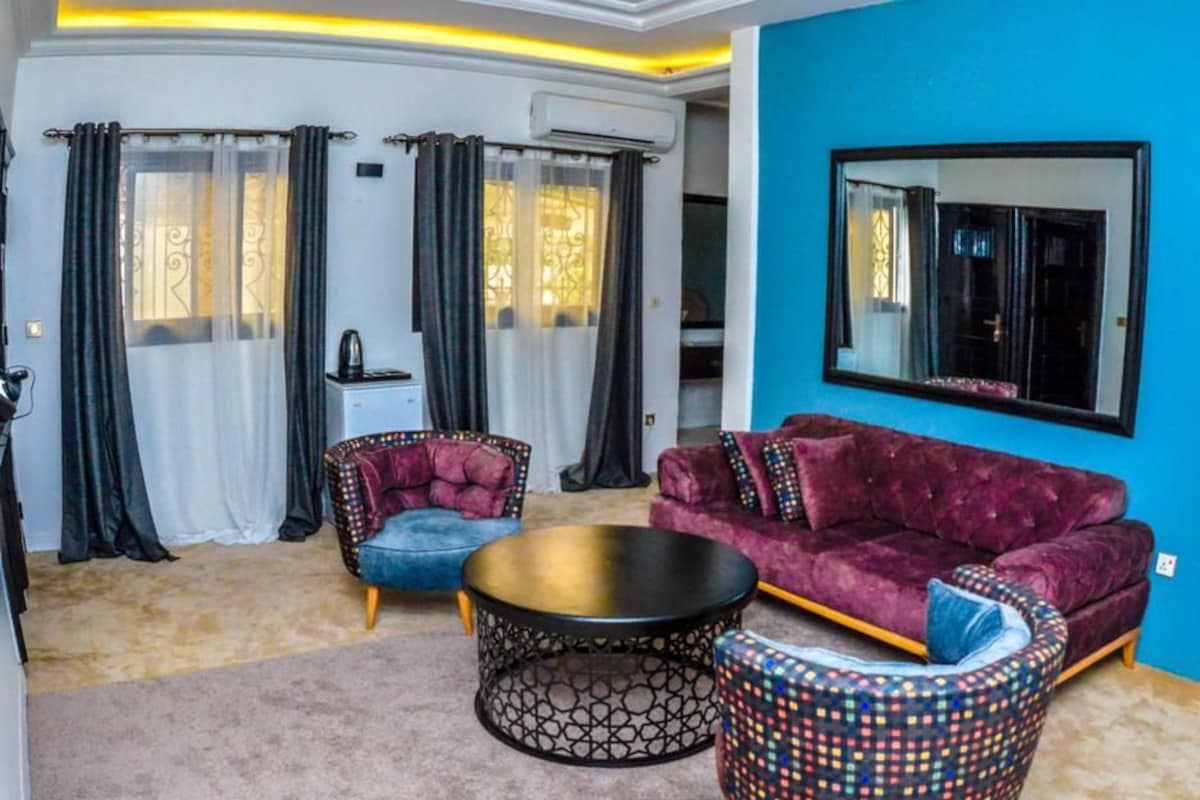 A modern living room with a purple sofa, two armchairs, a coffee table, and a patterned ottoman.