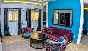 Una sala de estar moderna con un sofá púrpura, dos sillones, una mesita de centro y un reposapiés estampado.