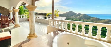 A spa area with a hot tub, outdoor seating, and a view of mountains and the sea.